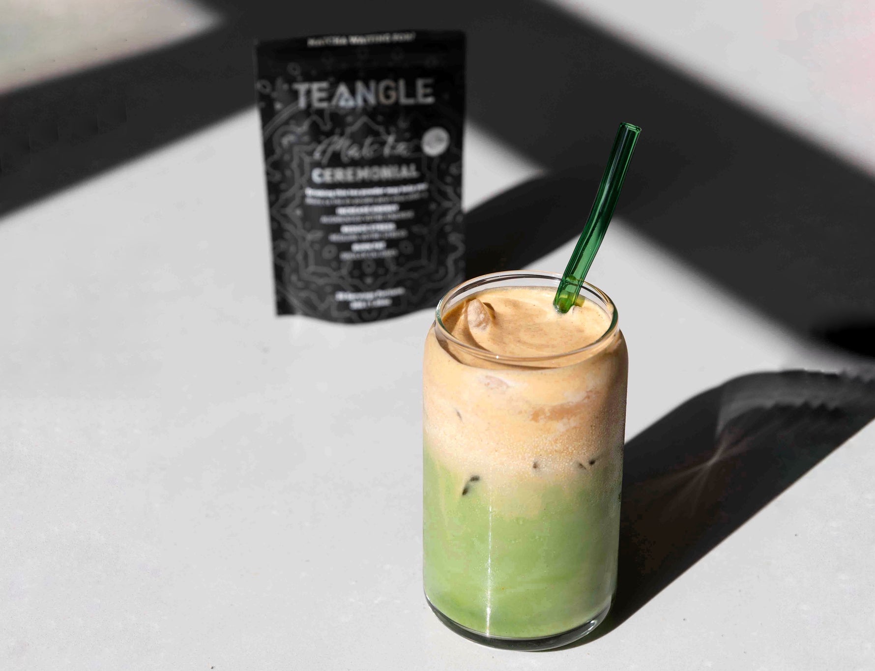 A tall glass filled with iced green matcha latte, crowned with a generous dollop of creamy pumpkin cold foam, sitting on a white counter